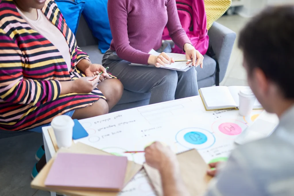 A group of professionals gather around a white coffee table and compare project notes